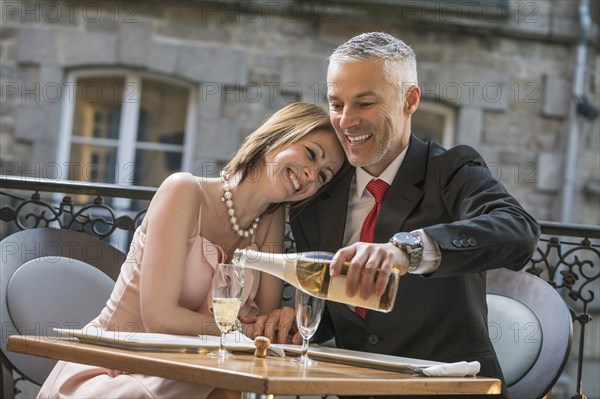 Well-dressed Caucasian man pouring champagne for woman