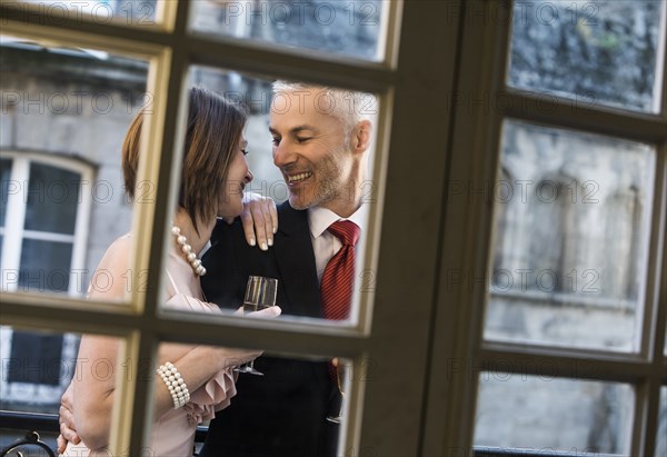 Well-dressed Caucasian couple drinking champagne behind window