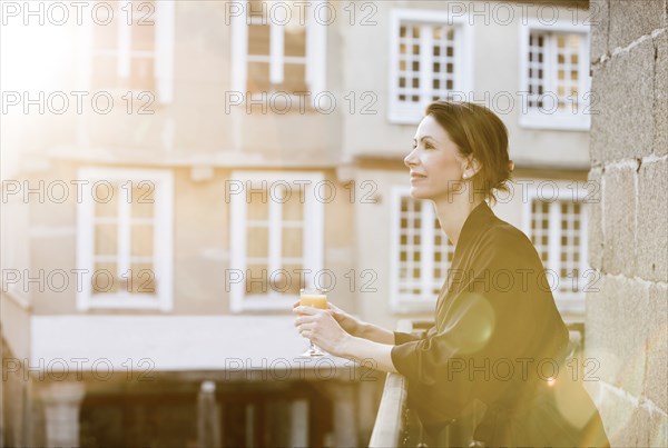 Caucasian woman drinking orange juice on balcony in city