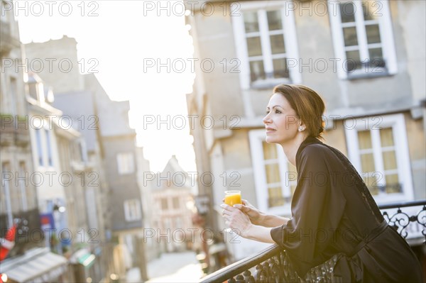 Caucasian woman drinking orange juice on balcony in city