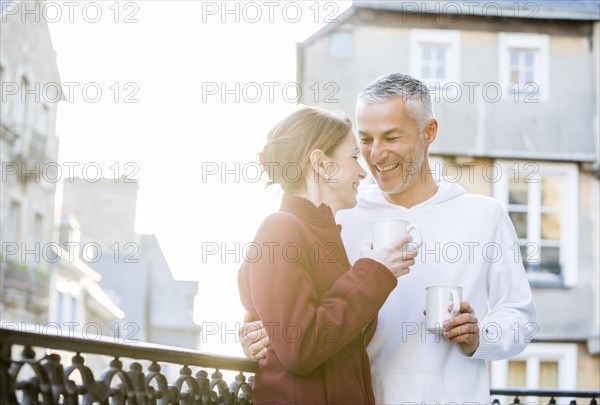 Caucasian couple drinking coffee on balcony in city