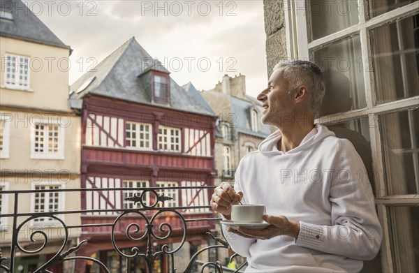 Caucasian man stirring coffee on balcony in city
