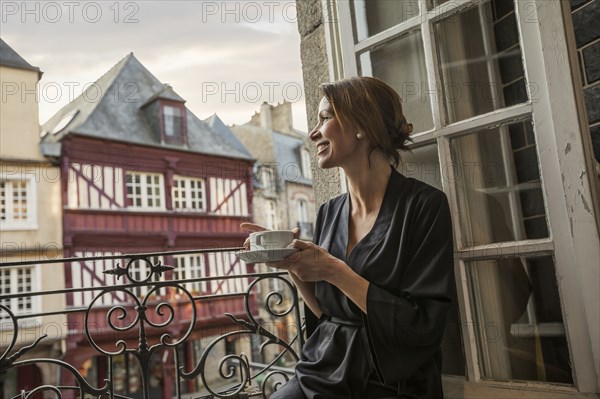 Caucasian woman drinking coffee on balcony in city