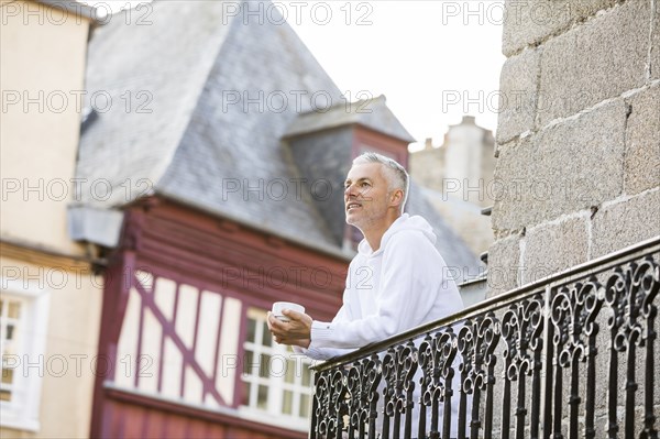 Caucasian man drinking coffee on balcony in city