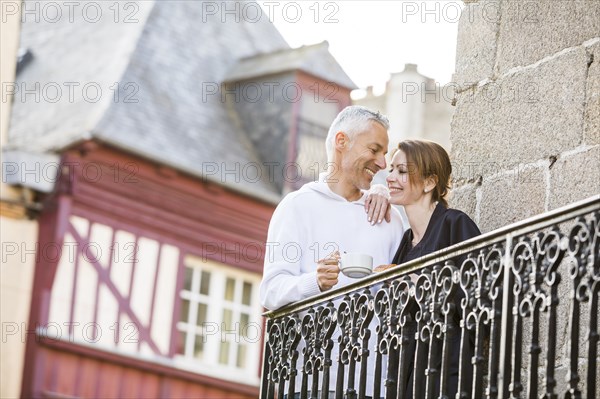 Caucasian couple drinking coffee on balcony in city