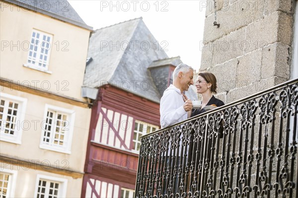 Caucasian couple drinking coffee on balcony in city