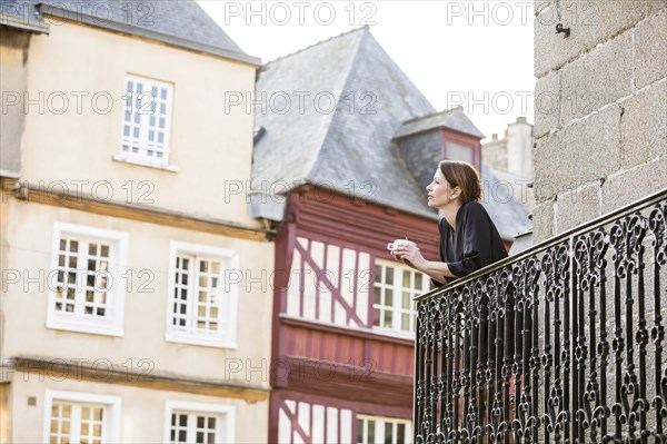 Caucasian woman drinking coffee on balcony in city