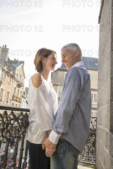 Caucasian couple holding hands on balcony in city