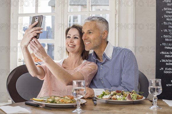 Caucasian couple posing for cell phones selfie in restaurant