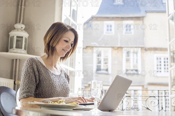 Caucasian woman typing on laptop and eating meal