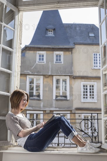 Caucasian woman sitting on windowsill using digital tablet