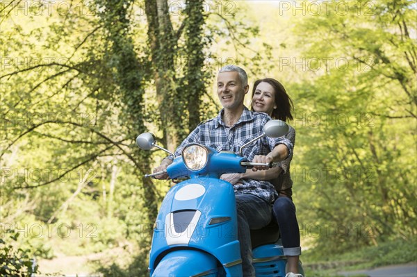 Caucasian couple riding blue motor scooter