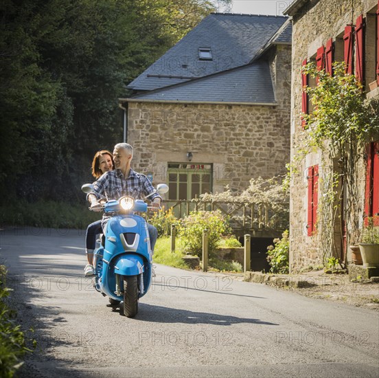 Caucasian couple riding blue motor scooter