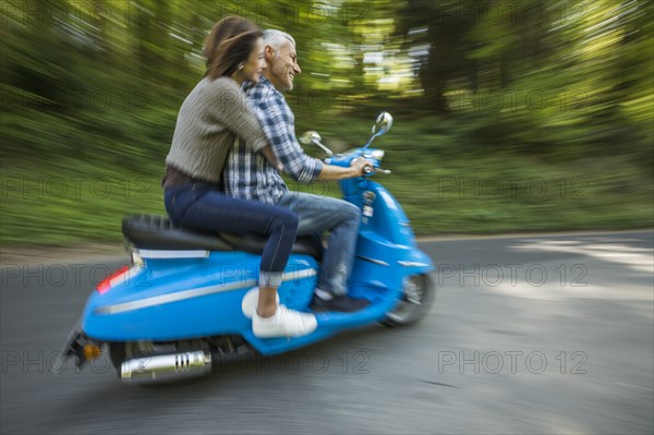 Caucasian couple riding blue motor scooter