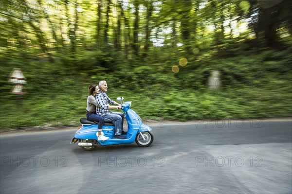Caucasian couple riding blue motor scooter