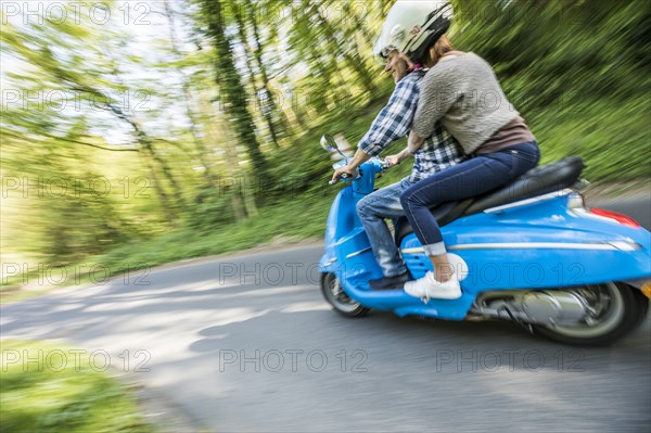 Caucasian couple riding blue motor scooter