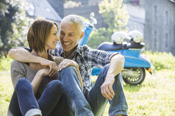 Caucasian couple sitting in grass near motor scooter