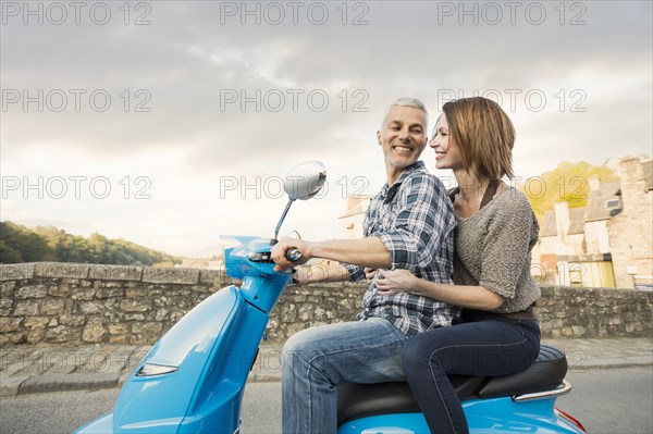 Caucasian couple riding blue motor scooter