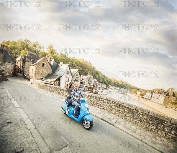 Carefree Caucasian couple riding blue motor scooter near river