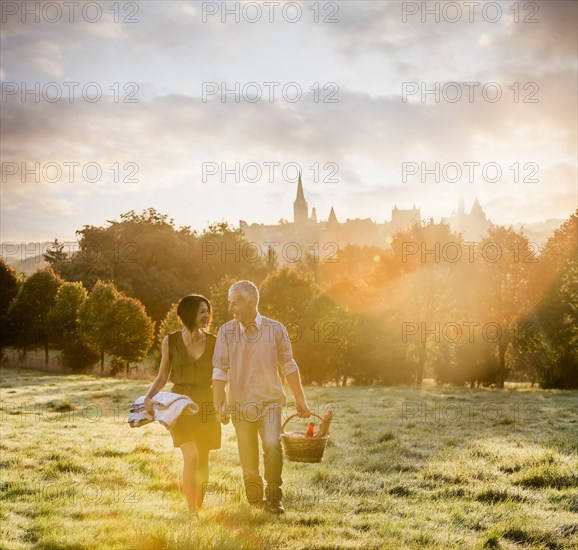 Caucasian couple walking in field carrying picnicblanket and basket