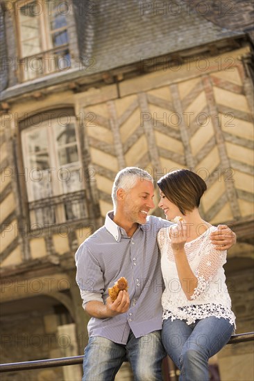 Caucasian couple eating bread on railing