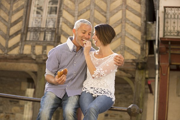 Caucasian couple eating bread on railing