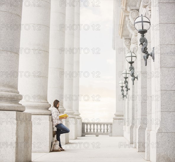 Caucasian woman leaning on pillar reading notebook