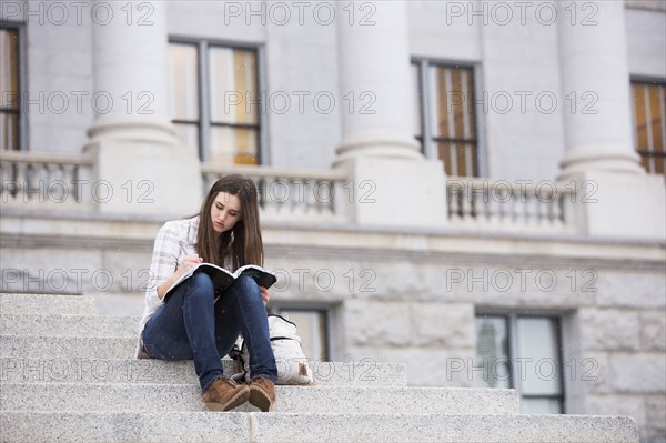 Caucasian woman sitting on staircase writing in notebook