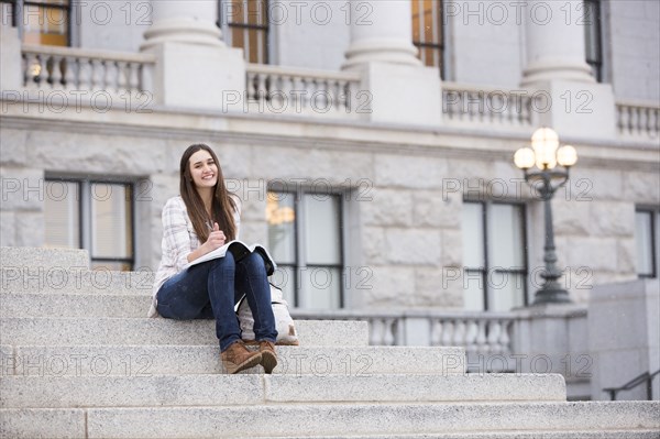 Smiling Caucasian woman sitting on staircase holding notebook