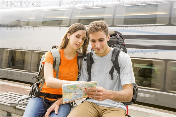 Caucasian couples sitting on bench near train reading map