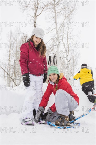 Caucasian mother adjusting snowshoe for daughter