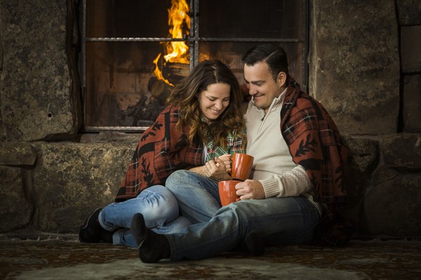 Smiling Caucasian couple cuddling on floor near fireplace