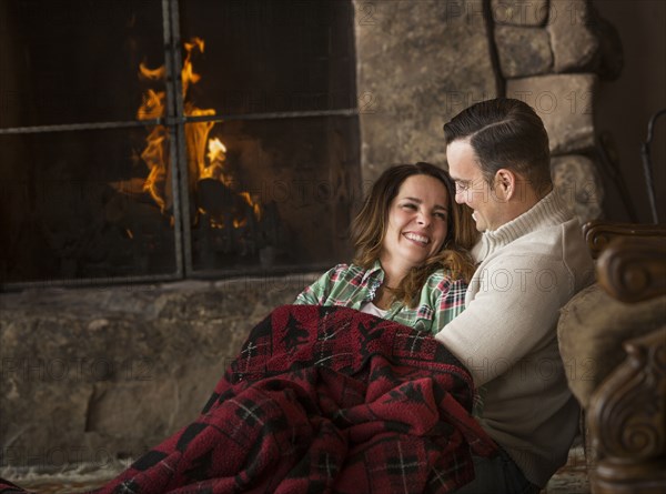 Smiling Caucasian couple cuddling on floor near fireplace