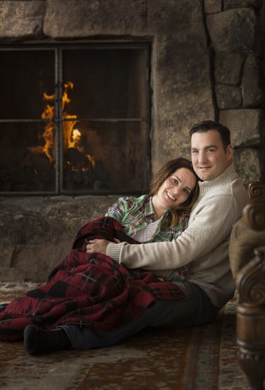 Smiling Caucasian couple cuddling on floor near fireplace