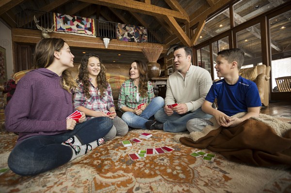 Caucasian family sitting on rug playing card game