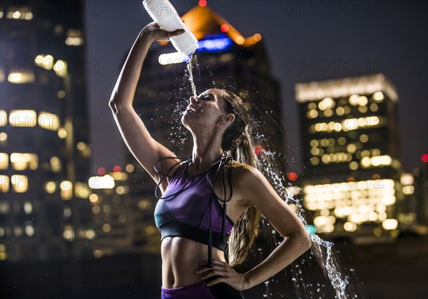 Caucasian woman spraying water on face in city at night