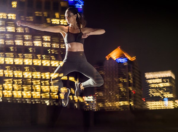 Double exposure of Caucasian woman jumping in city at night