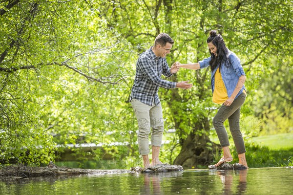 Man helping woman standing on rocks crossing river