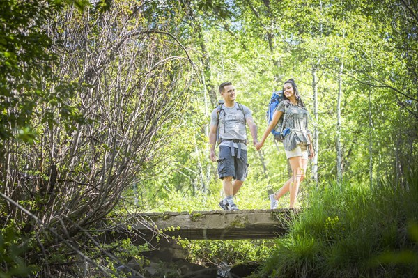 Couple carrying backpacks across bridge in woods