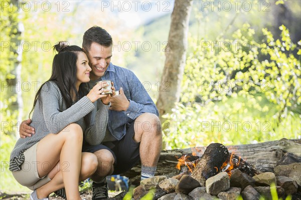 Couple drinking coffee near campfire