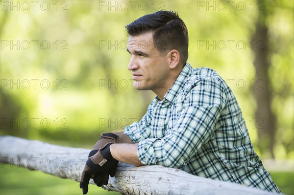 Man wearing gloves leaning on wooden fence