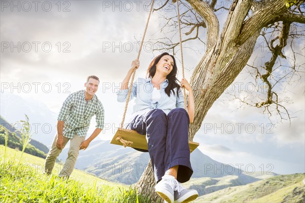 Man pushing woman swinging on tree swing