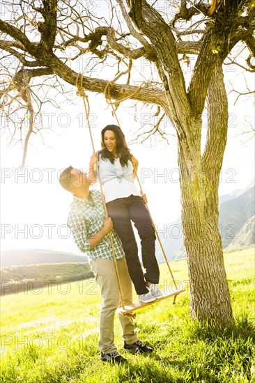 Man holding woman on tree swing
