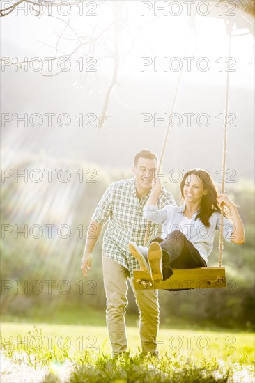 Man pushing woman swinging on tree swing