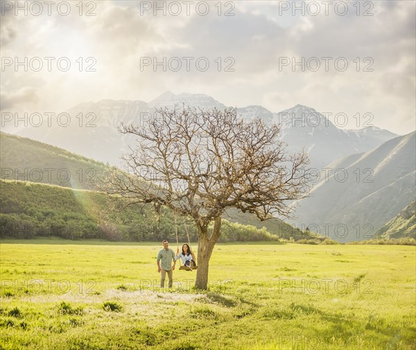 Man pushing woman swinging on tree swing