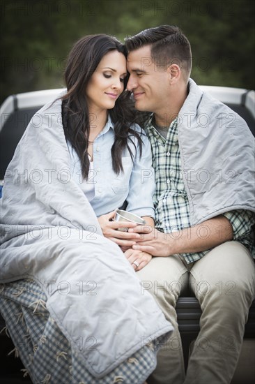 Couple wrapped in blanket sitting on bed of pick-up truck