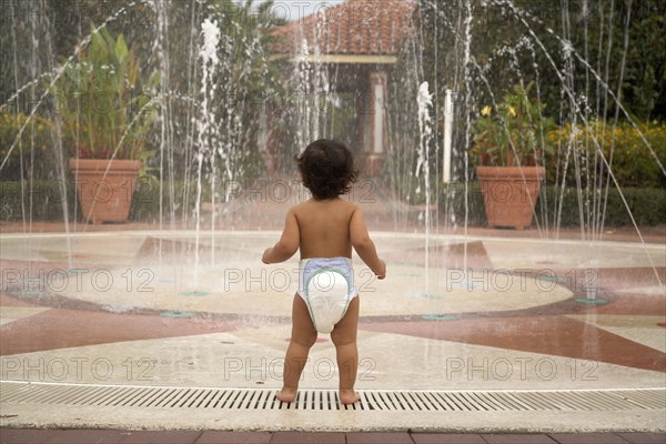 Mixed race baby wearing diaper standing near fountain