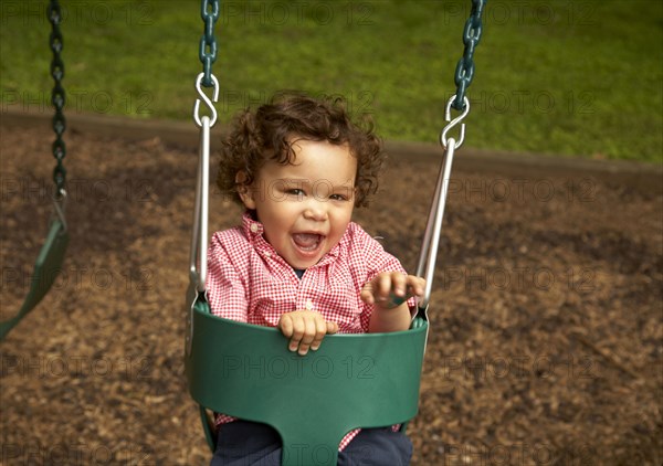 Mixed race child sitting in swing laughing