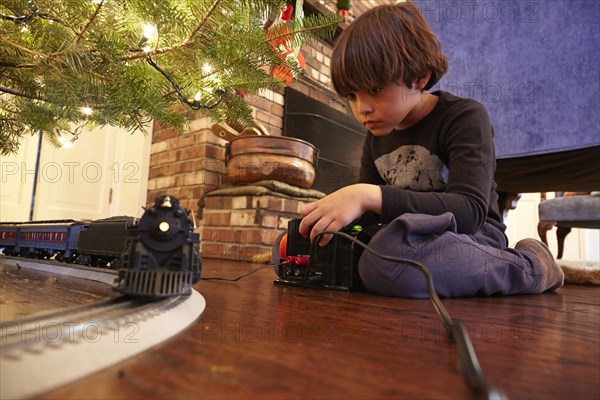 Mixed race boy playing with train under Christmas tree