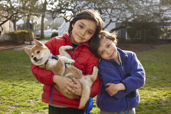 Mixed race siblings holding puppy in backyard